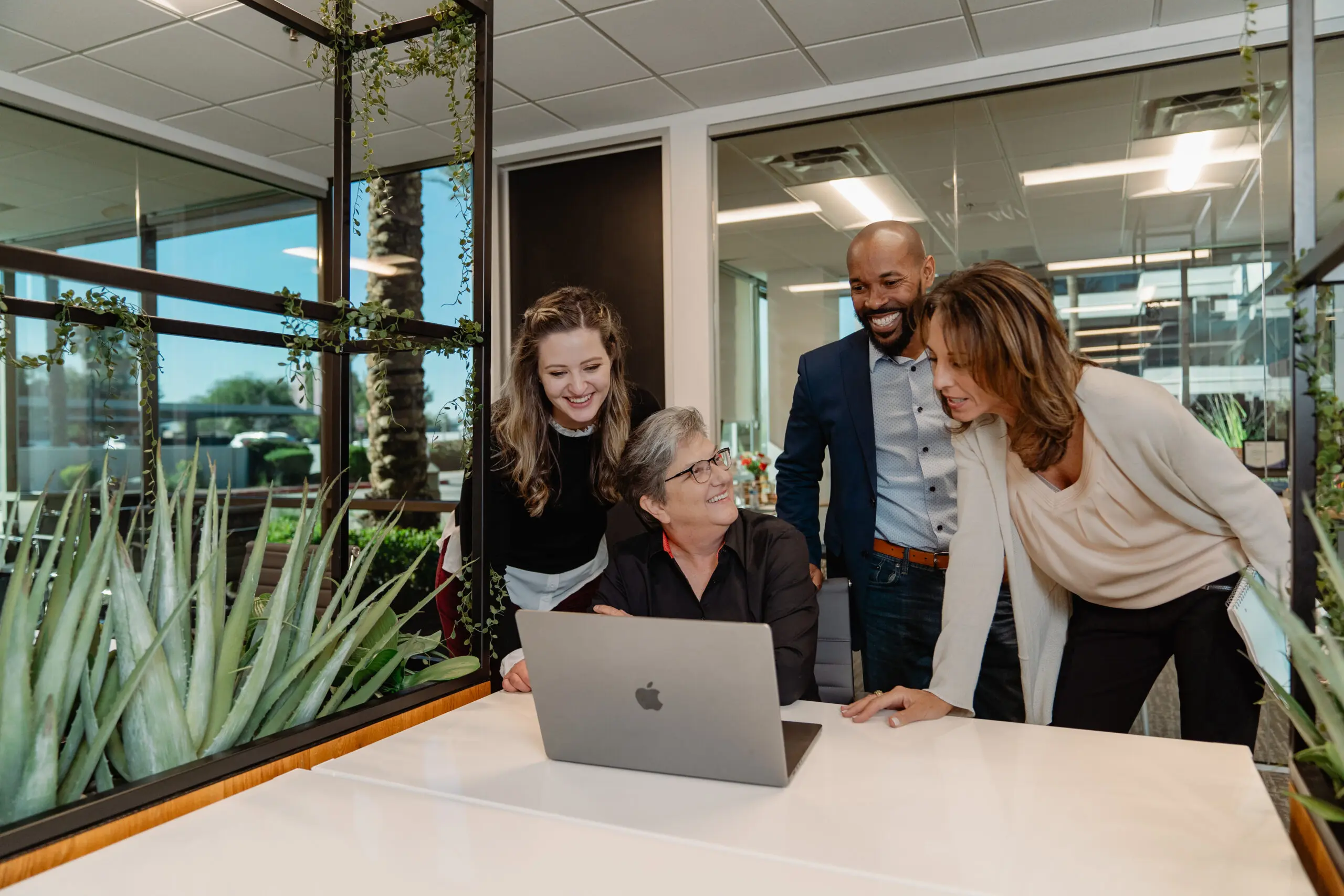 Four individuals working together around a laptop computer smiling and delegating effectively
