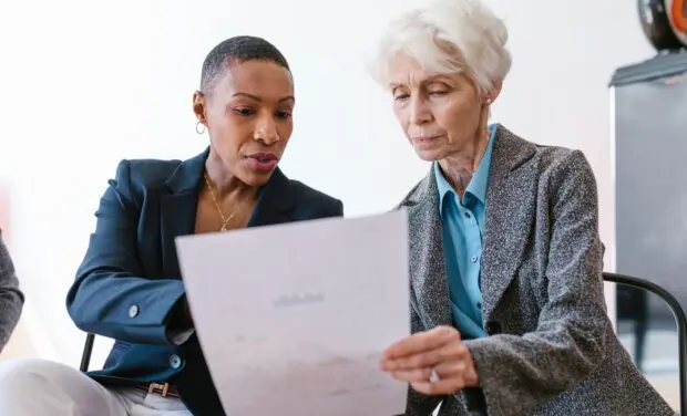 Two professional women review a document together in a office setting.