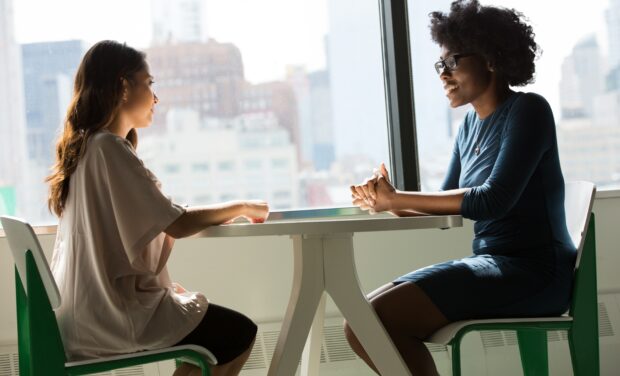 Two women sitting in front of a window facing each other at a small table engaging in a coaching conversation